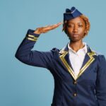female aircrew member doing military salute studio showing gratitute country camera young stewardess with professional occupation wearing aviati